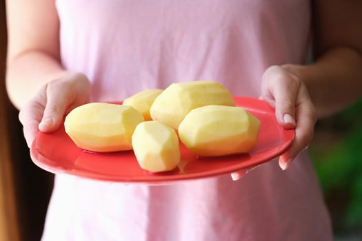 Woman housewife holding plate of peeled potatoes in her hands closeup. Potato recipes concept