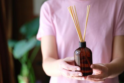 Woman holding jar with bamboo sticks of air freshener for home closeup. Aromatherapy concept