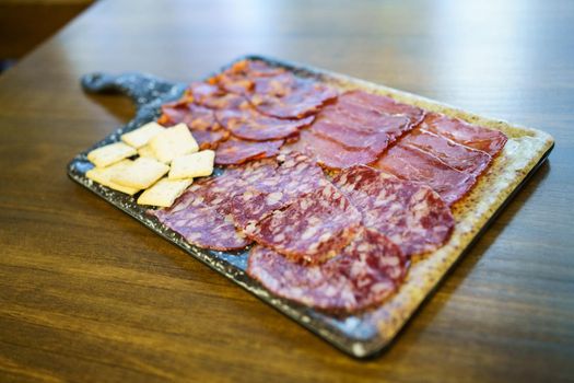 Iberian cured meats platter. A typical dish of Spanish cuisine. with crackers placed on board on lumber restaurant table