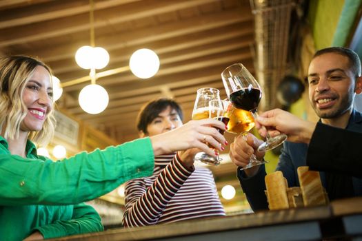 From below happy diverse male and female friend clinking glasses of alcohol during party in weekend in pub