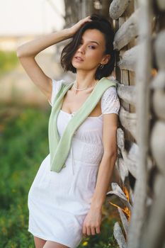 Pretty young Asian woman, posing near a tobacco drying shed, wearing a white dress and green wellies. Beauty and fashion concept