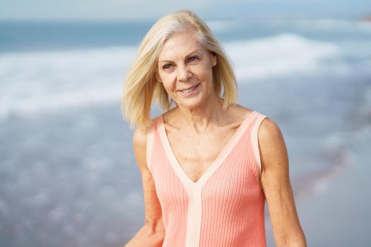 Mature woman enjoying her free time looking at the sea from the shore of the beach.. Elderly female enjoying her retirement at a seaside retreat.