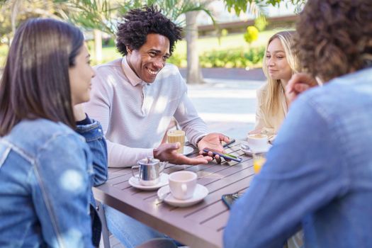 Company of positive diverse friends sitting at table in summer cafe and enjoying meeting while looking at each other