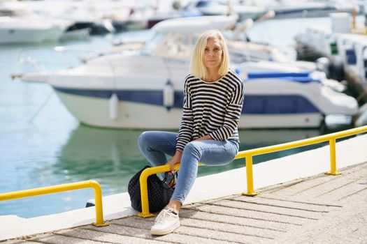 Mature woman looking serenely at the camera, sitting in a seaport.