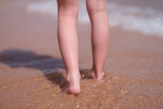 Bare feet of child walking along sea shore closeup. Holidays at resort with children concept