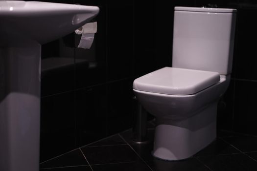 White toilet standing in bathroom with black tiles. Sale of quality sanitary ware concept