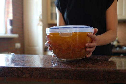 Housewife holding plastic container with soup in her hands closeup. Food storage at home concept