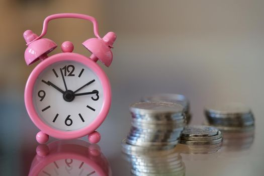Pink alarm clock standing near pile of coins closeup. Time to make money concept