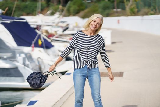Happy woman in her 60s strolling along a seaside spot near the beach. Elderly female enjoying her free time.
