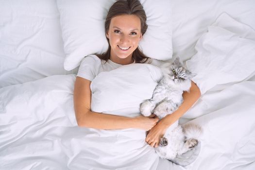 Beautiful woman lying on the bed and hugging her lovely cute cat. Sleeping with cat. High quality photo