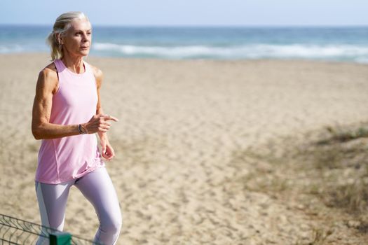 Mature woman running along the shore of the beach. Older female doing sport to keep fit. Concept of healthy living in the elderly. Senior woman in fitness clothing running along beach