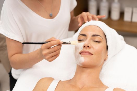 Aesthetics applying a mask to the face of a Middle-aged woman in modern wellness center. Beauty and Aesthetic concepts.