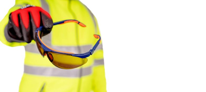 A construction worker in a bright yellow hi-viz coat and red safety gloves giving tinted safety glasses to the viewers for eye protection isolated on white background. Safety on construction site banner concept