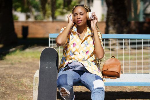 African woman with skateboard. Black girl relaxing after riding skateboard listening to the music outdoors.
