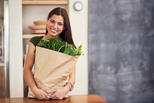 Portrait of an happy young woman holding a bag of groceries in her kitchen.