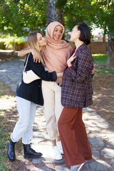 Group of young multiethnic girls best friends in casual clothes smiling and looking at camera while cuddling in park on sunny day
