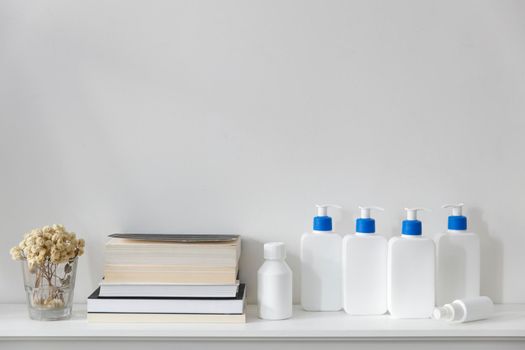 White bottles with a blue dispenser with shampoo, conditioner, cream and liquid soap, figurines stand on a shelf in the bathroom. Place for text.