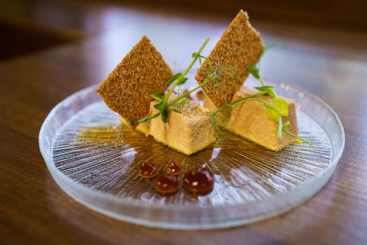 Plate of foie micuit with crispy croutons and drops of marmalade on a wooden table in a fine dining restaurant.