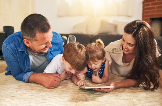 Shot of an adorable brother and sister using a digital tablet with their parents on the floor at home.