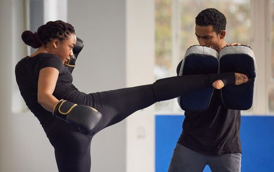 Shot of a young woman practicing kickboxing with her trainer in a gym.