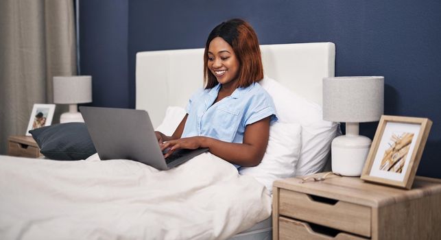 Cropped shot of an attractive young woman using her laptop while sitting in bed.