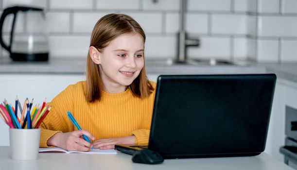 Preteen girl with laptop studying during remote lesson. Pretty schoolgirl learning with pc and having class online with new technologies at covid time