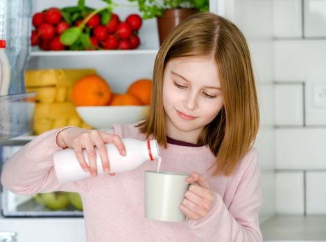 Pretty preteen girl filling cup mug with yogurtat kitchen at home. Beautiful female kid with milk products
