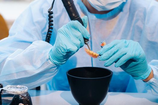 A masked and gloved dental technician works on a prosthetic tooth in his lab.