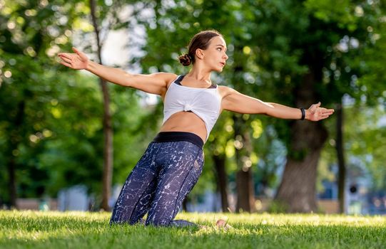 Girl doing yoga at nature and training her balance. Young woman exercising and stertching in summertime