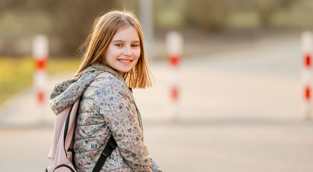 Preteen girl child with backpack outdoors. Pretty schoolgirl going home after class and smiling