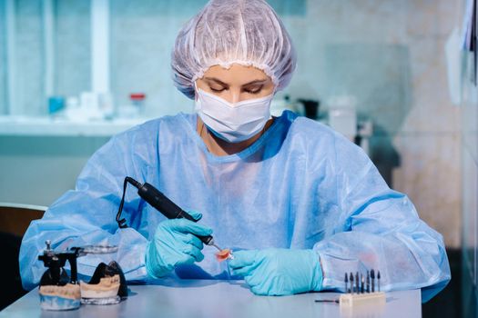 A dental technician in protective clothing is working on a prosthetic tooth in his laboratory.