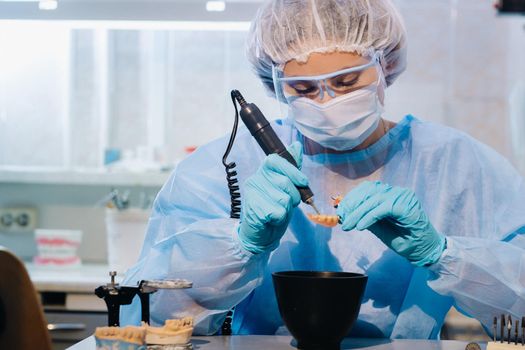 A dental technician in protective clothing is working on a prosthetic tooth in his laboratory.