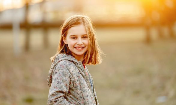 Preteen girl child looking at camera and smiling in amazing sunset light in the field. Beautiful portrait of pretty female kid