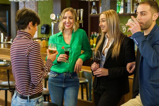 Cheerful women listening to girlfriend near man drinking beer from glass while resting in pub on weekend day together