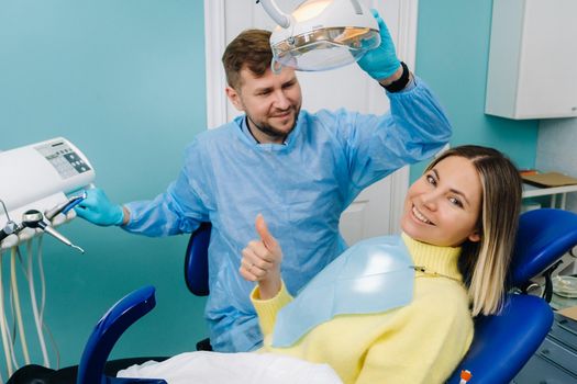 Beautiful girl patient shows the class with her hand while sitting in the Dentist's chair.