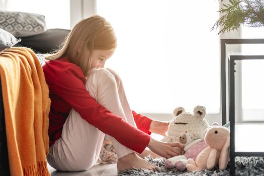 Preteen girl playing with toys on floor at home A teenager sits at room with large window next to sofa