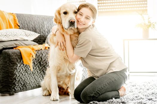 Pretty girl hugging golden retriever dog at home sitting on floor. Happy teenager with purebred doggy pet labrador in cozy room with daily light