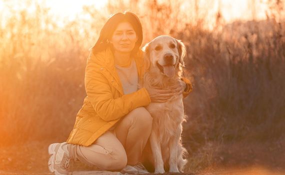 Girl hugging golden retriever dog with sunset light outdoors. Young woman petting doggy pet labrador at nature at autumn