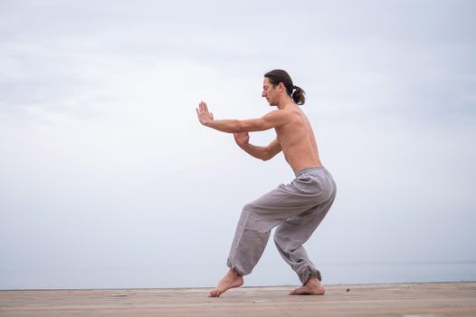 Caucasian man with naked torso practicing wushu on the seashore