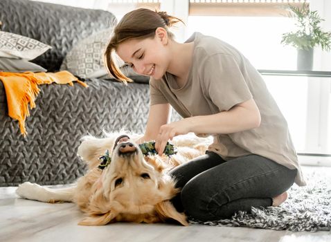 Pretty girl playing with golden retriever dog at home sitting on floor. Happy teenager with purebred doggy pet labrador in cozy room with daily light