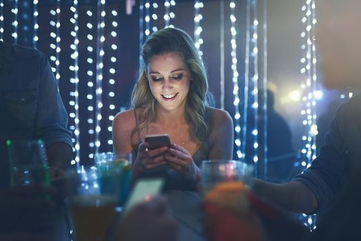 Shot of a young woman texting on her smartphone while sitting in a crowded nightclub.