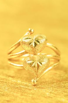 A Heart shaped gold ring on golden coloured background.