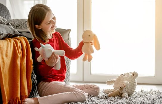 Happy child girl playing with plush toys. Cheerful kid having fun while sitting on the floor