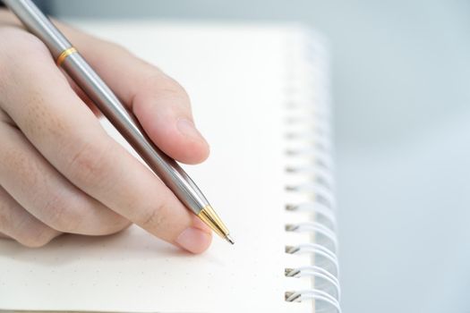 Businesswoman writing on notebook in office, hand of woman holding pen with writing notebook on desk