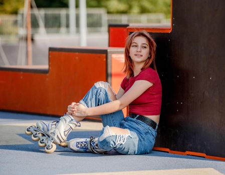 Beautiful girl wearing roller skates sitting on ground and looking back. Pretty female teenager skater portrait