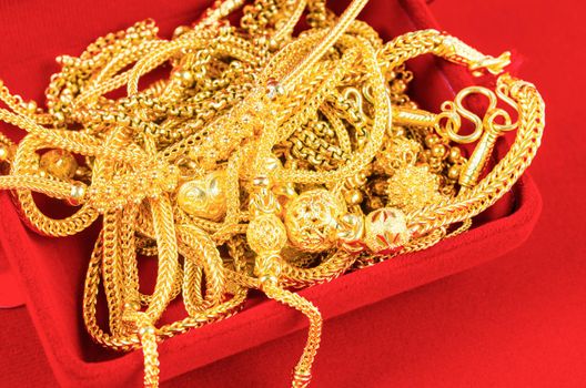 The many gold necklaces in a red velvet box on red background.