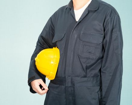 Worker standing in blue coverall holding yellow hardhat isolated on blue background