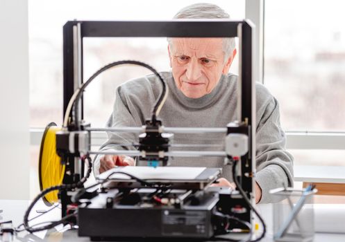 Adult man preparing 3D printer and its components for work on project in labaratory