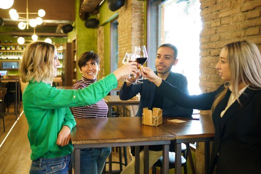 Happy diverse group of friends clinking glasses of alcohol during party in weekend in pub