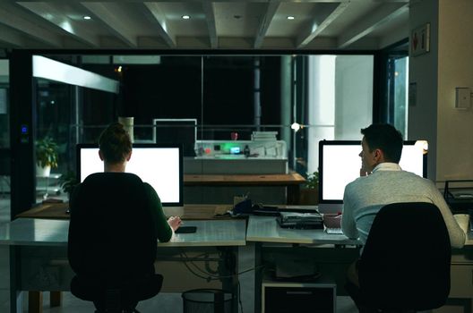 Rearview shot of two businesspeople working on computers in an office at night.